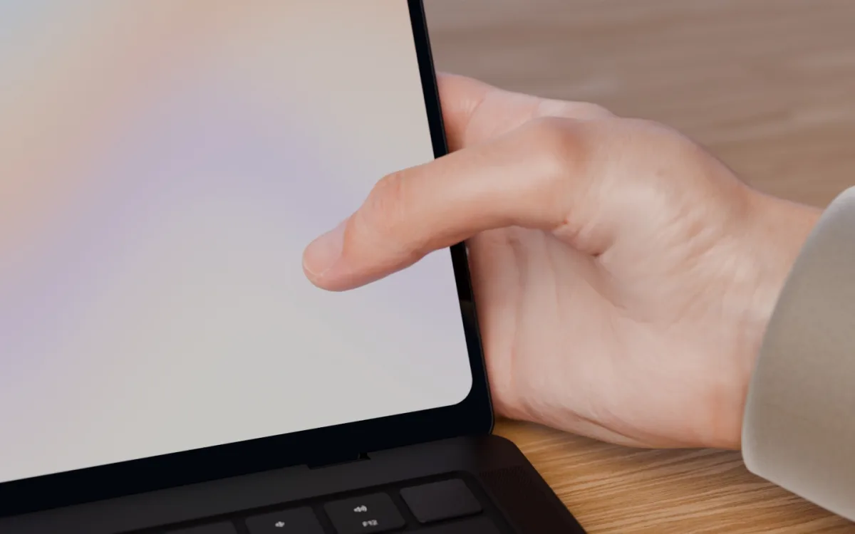 A hand holds the MacBook's lid by its edge, thumb resting on the screen.